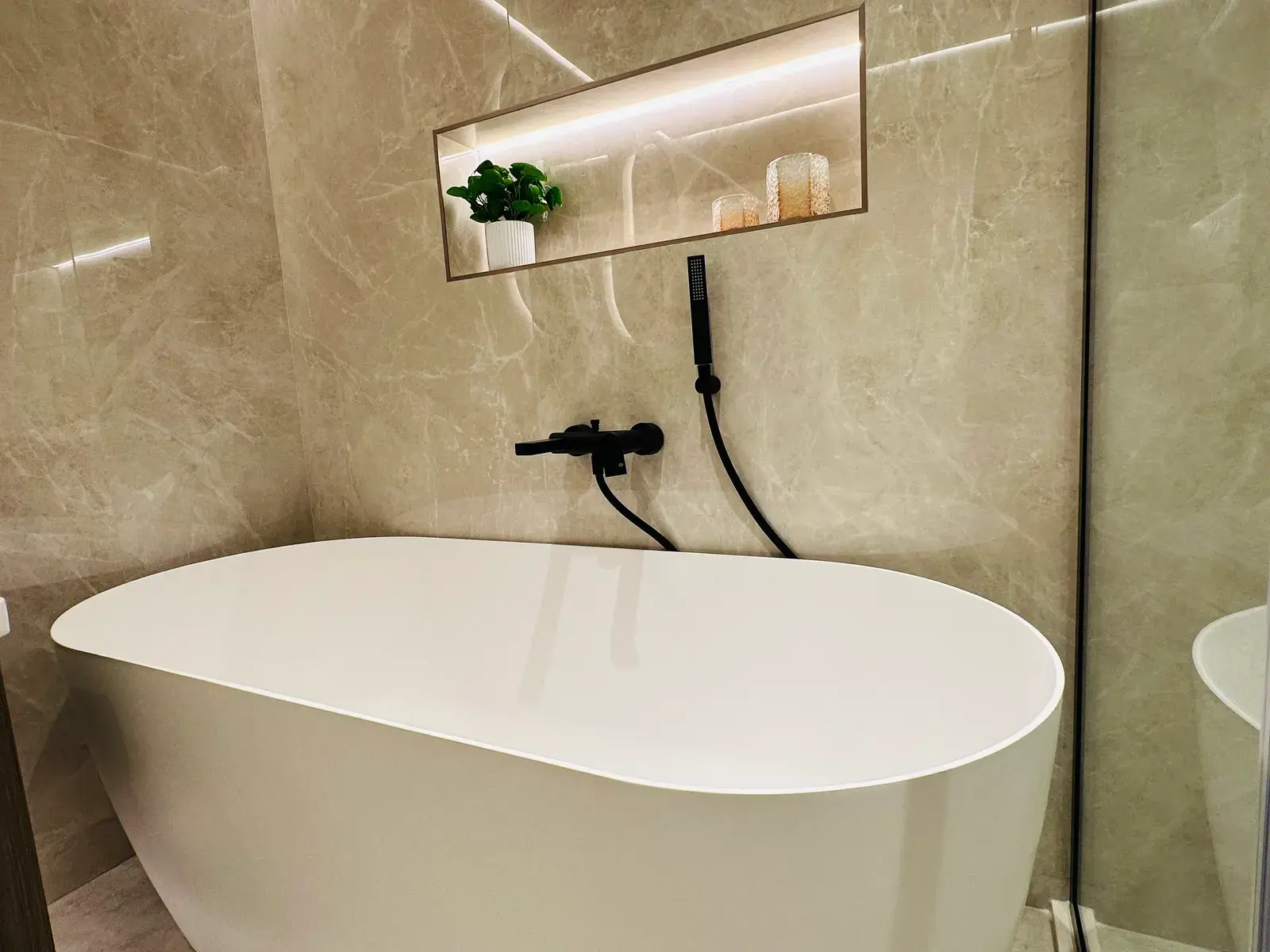 Freestanding oval bath against a full-height stone wall with a lit niche