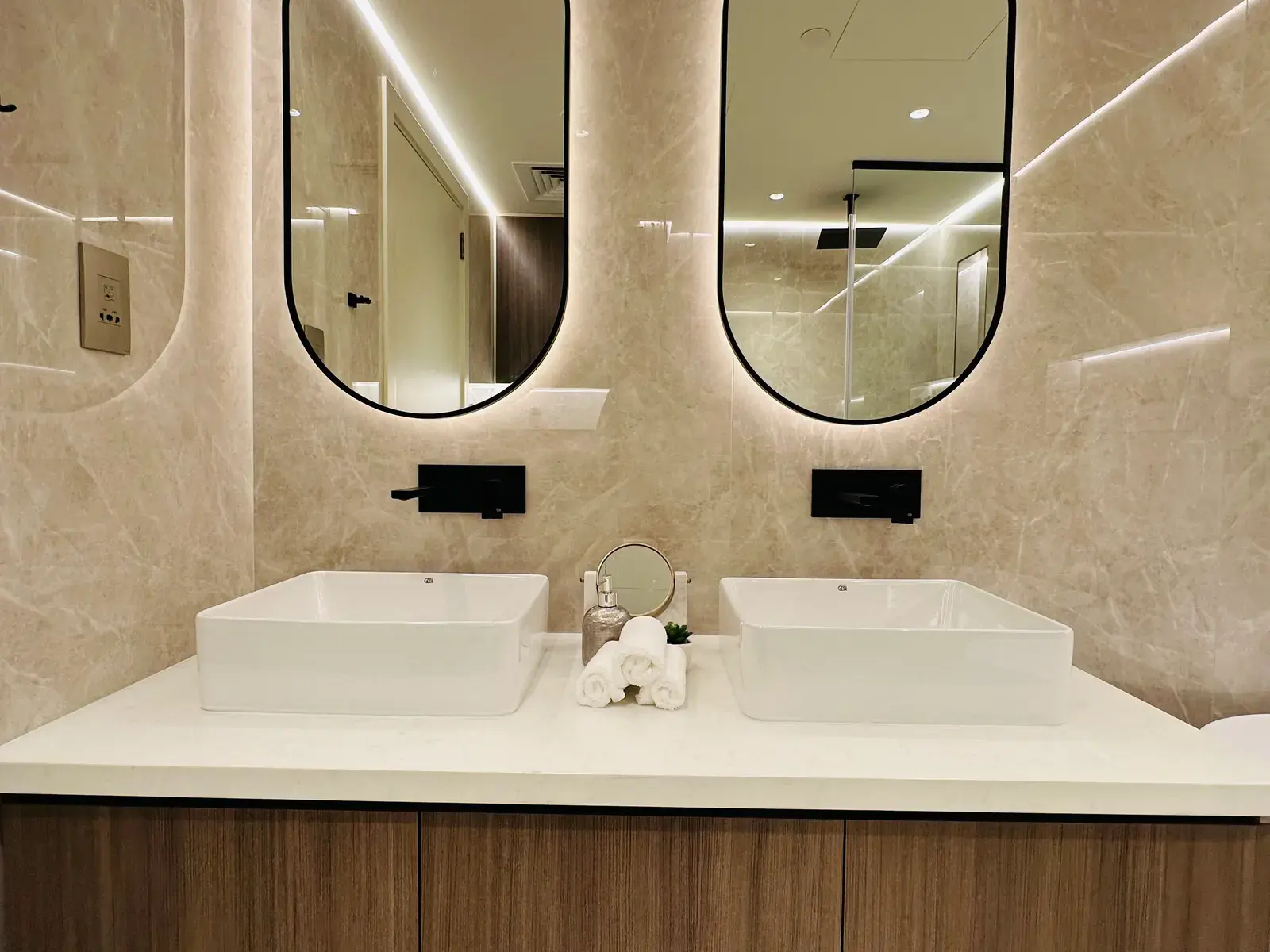 Twin counter-top basins on a walnut vanity beneath two arched backlit mirrors