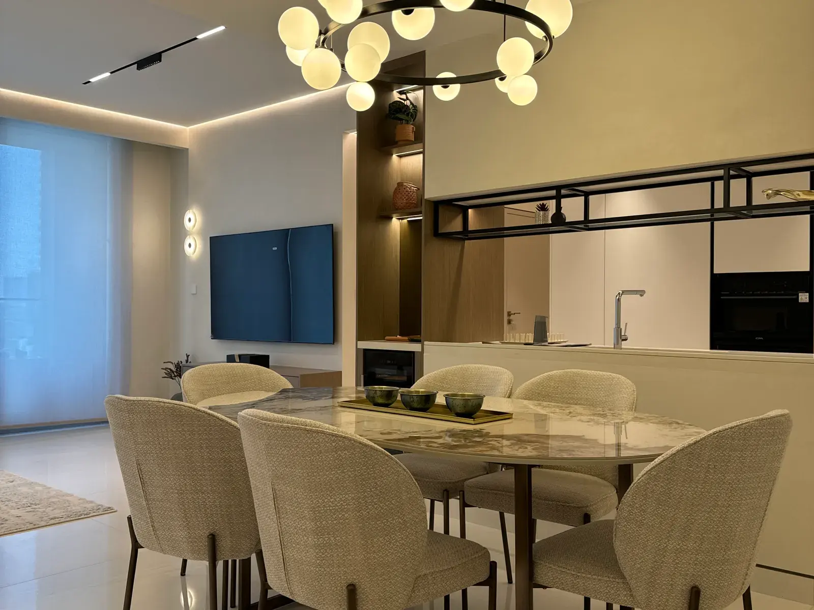 Open-plan living and dining room with a sculptural chandelier and bronze-framed screen