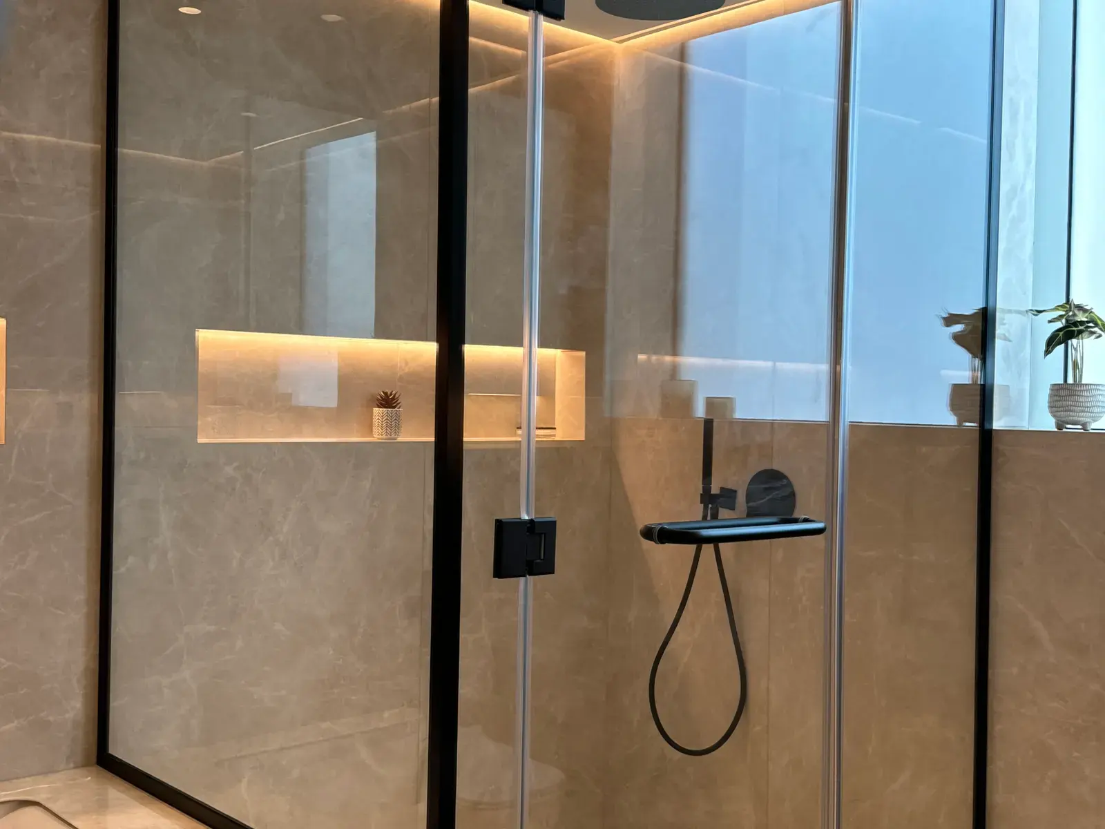 Walk-in shower behind a black-framed glass screen with a lit niche