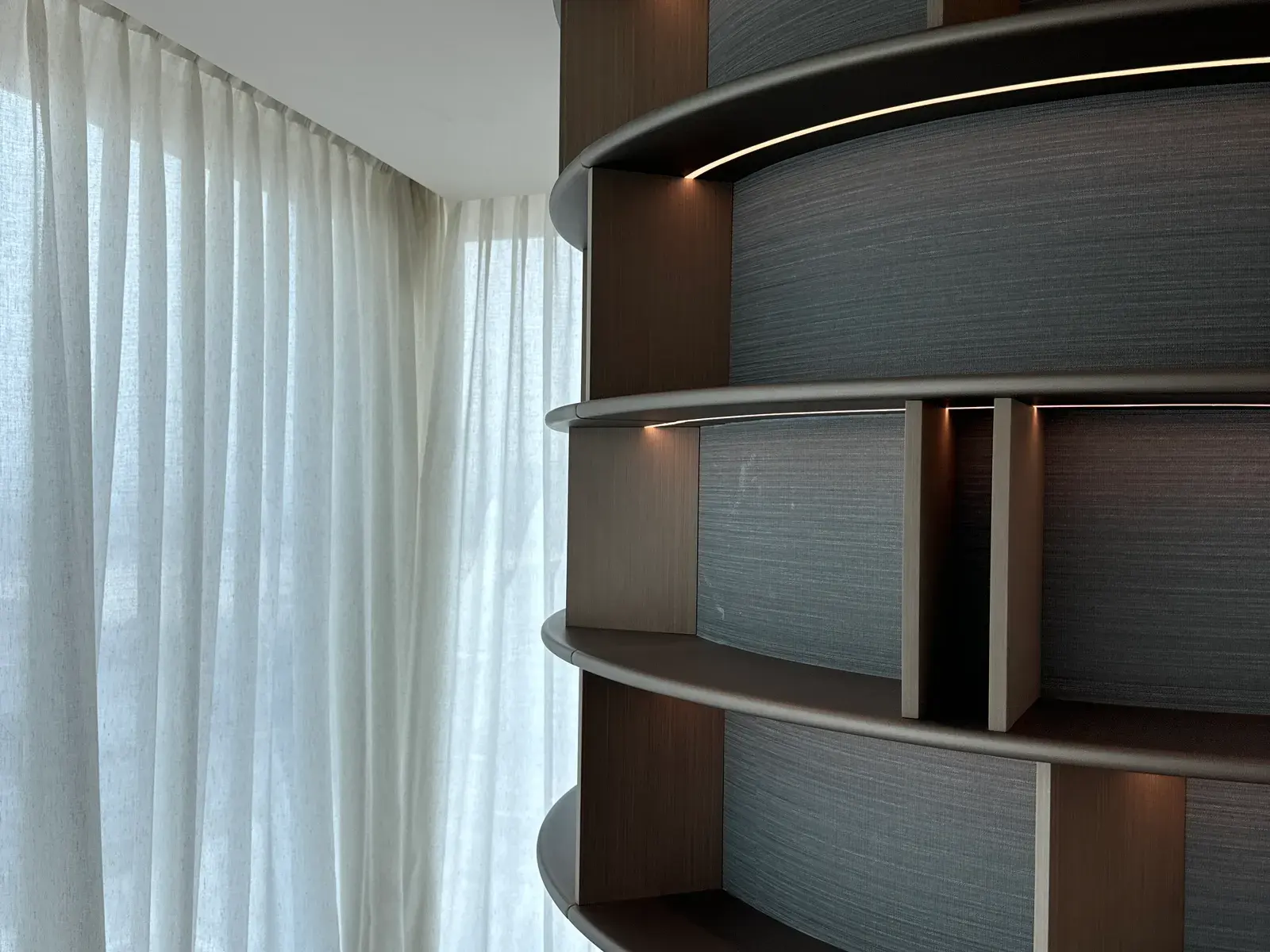 Curved shelving unit in tinted timber with lit display bays