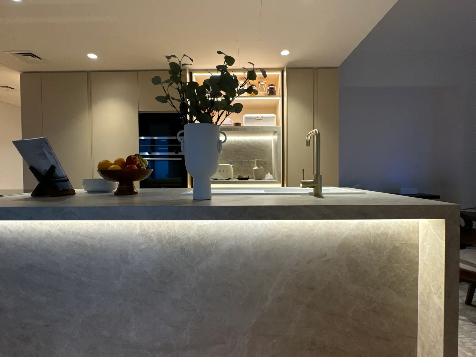 Stone kitchen island lit from the plinth with integrated appliances behind