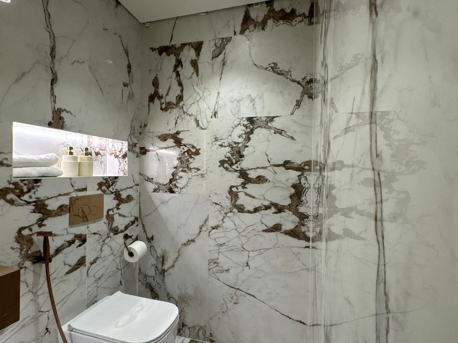 Bathroom lined in book-matched marble with a lit niche