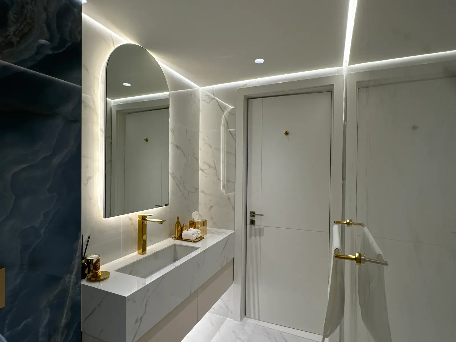 Marble vanity with an arched mirror backlit into the stone wall