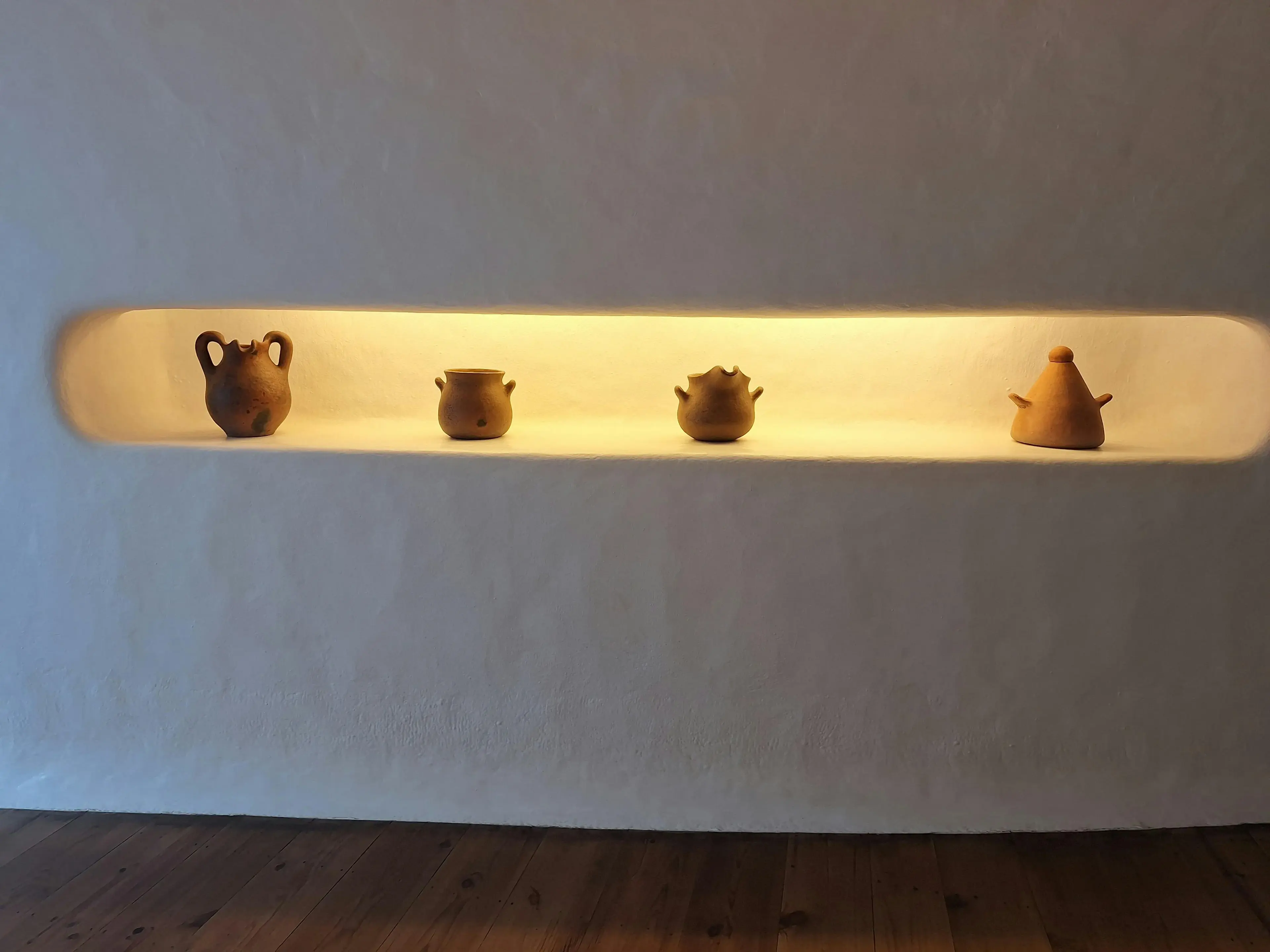 Illuminated gypsum wall niche with concealed LED lighting displaying ceramic vessels in Dubai