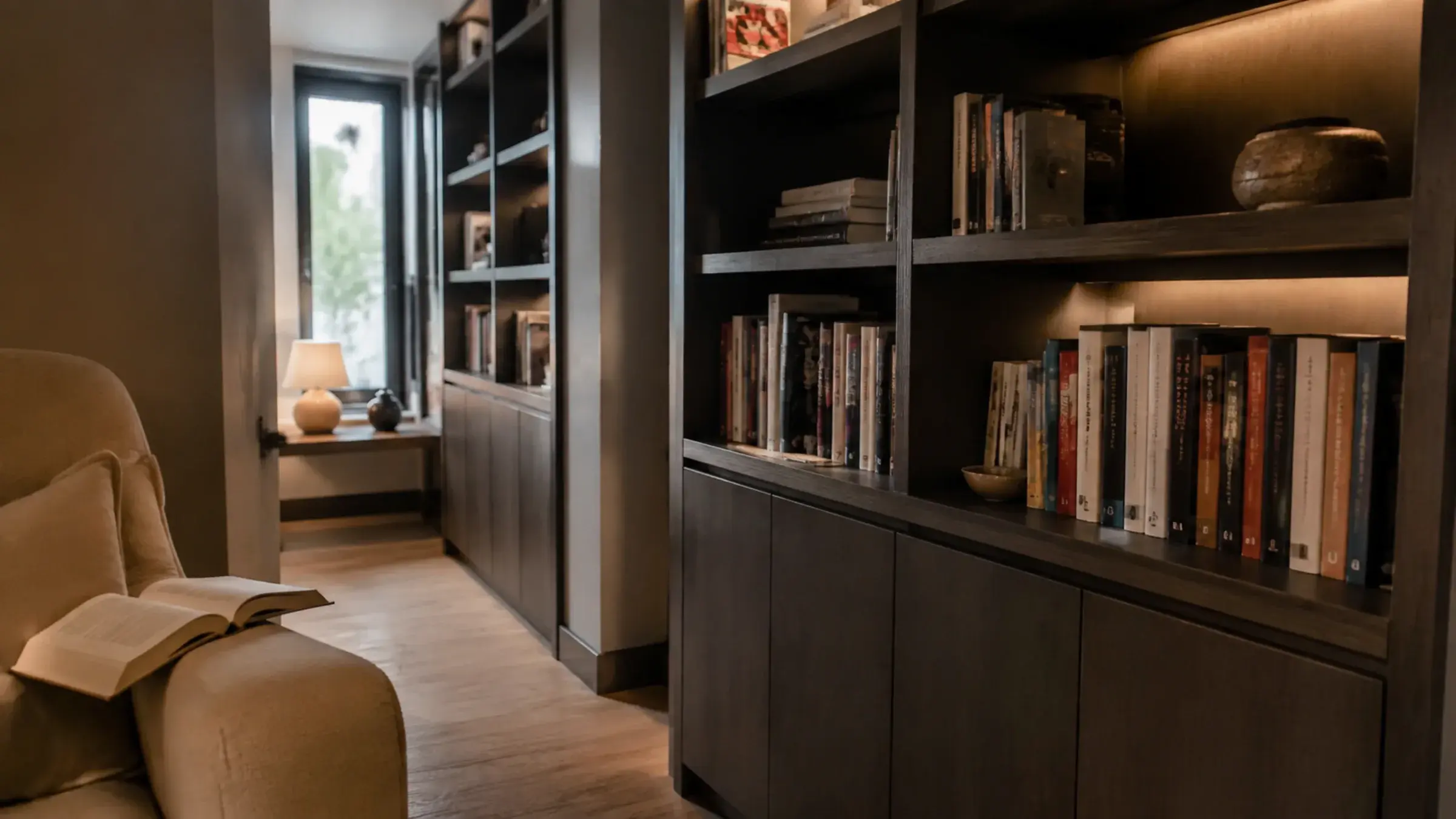 Home library corner with floor-to-ceiling built-in shelving and a reading chair, a book left open face-down on the arm