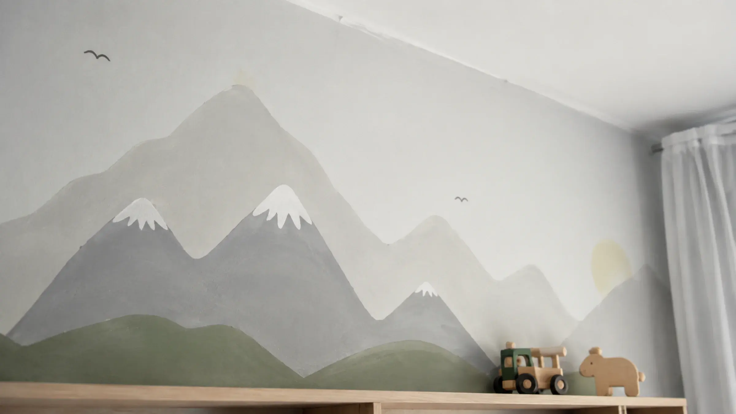 Hand-painted mural feature wall in a kids' bedroom with visible brush texture, a shelf with a few toys at the bottom edge