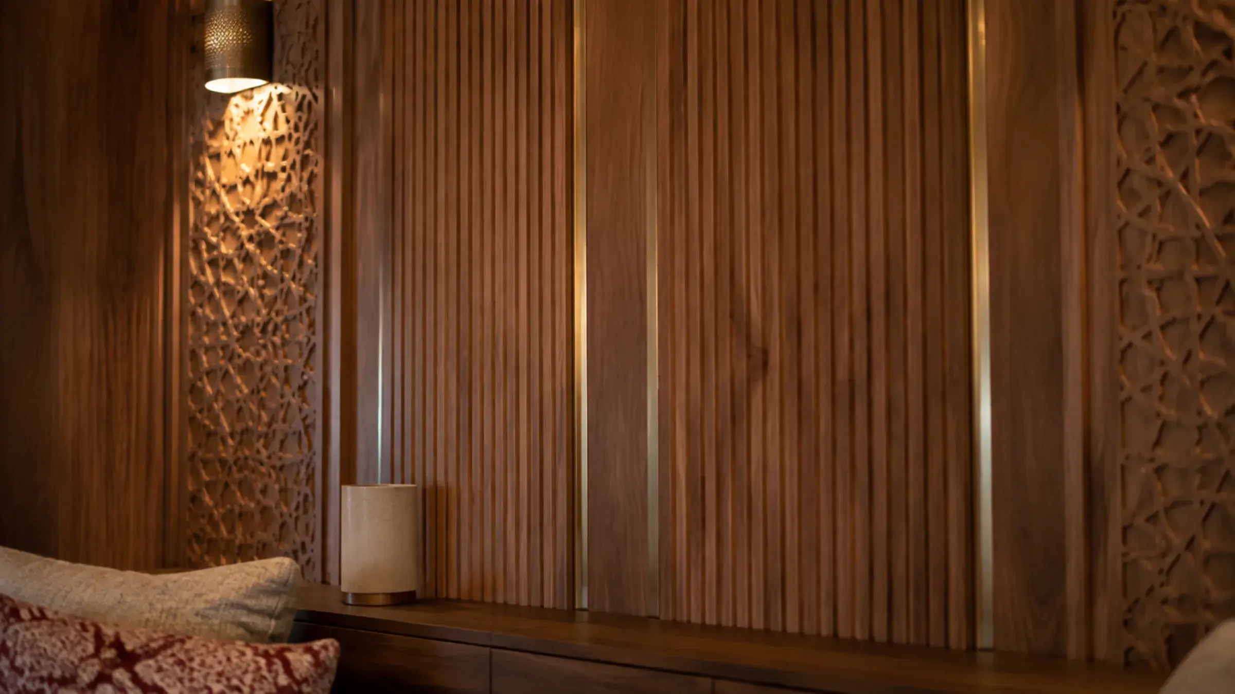 Fluted walnut wall panelling with a brass reveal and a carved geometric star panel lit by a wall sconce