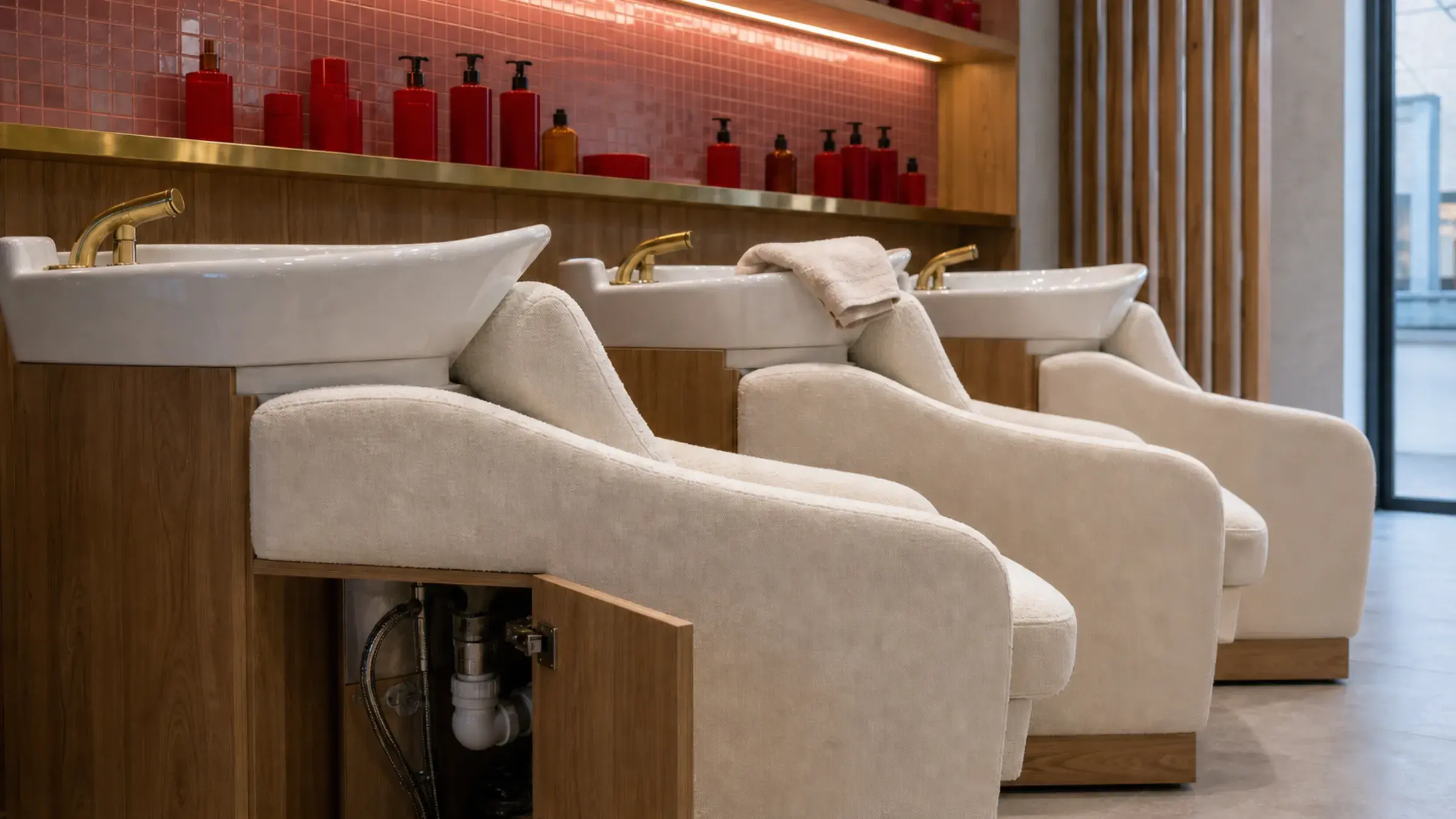 Cream salon backwash chairs and white basins with an open service panel exposing the drainage trap