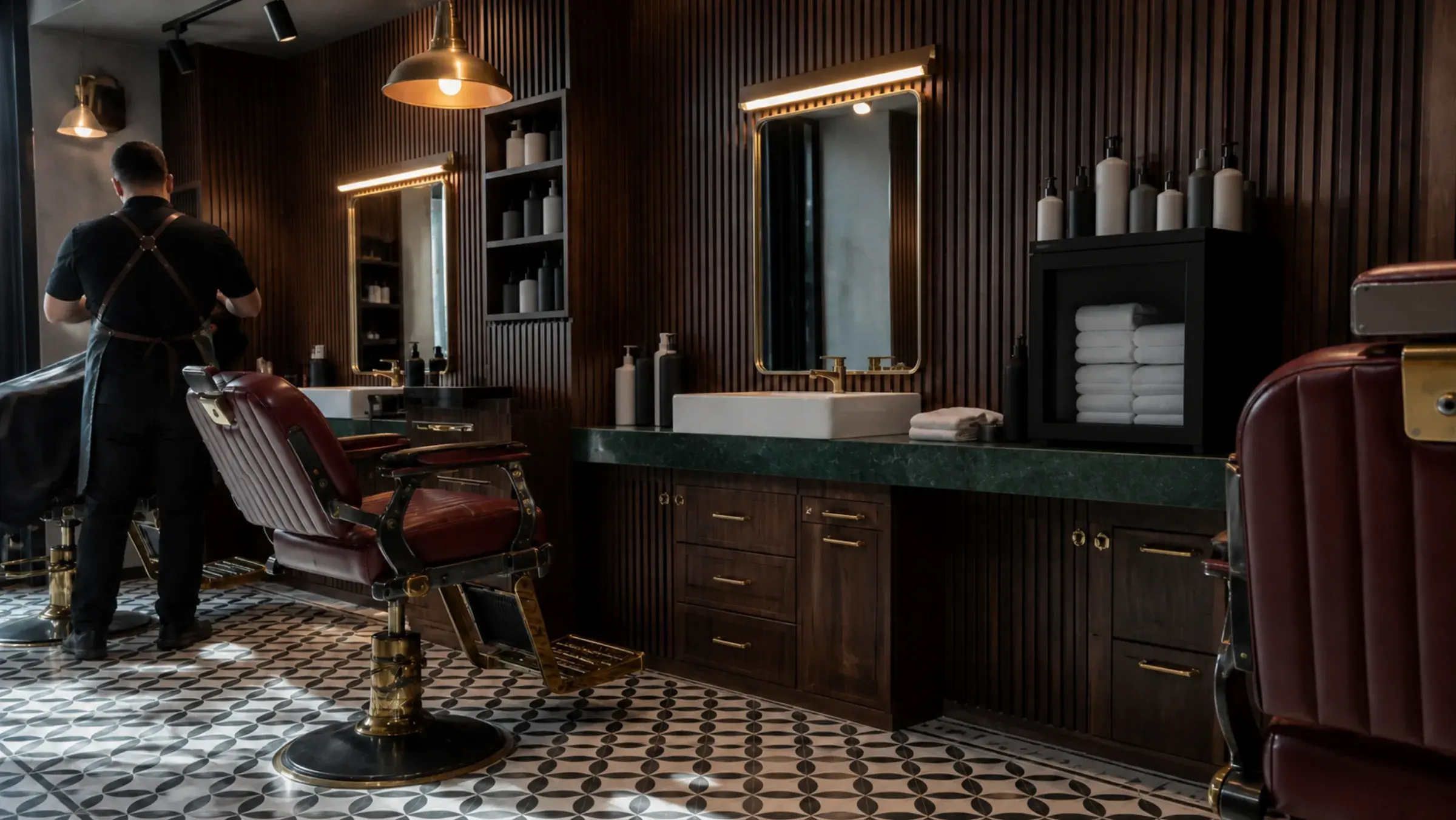 Oxblood barber chairs and brass-framed stations against dark walnut panelling in a gents salon