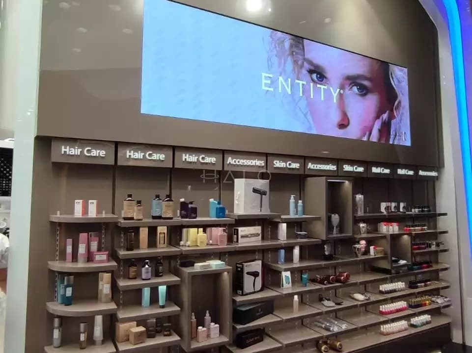 Salon retail display wall in Dubai with lit product shelving, category signage and a digital screen
