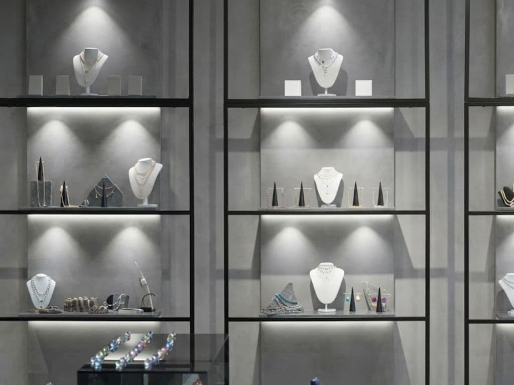 Accent-lit display shelving with concealed strip lighting rendering jewellery against a pale plaster wall