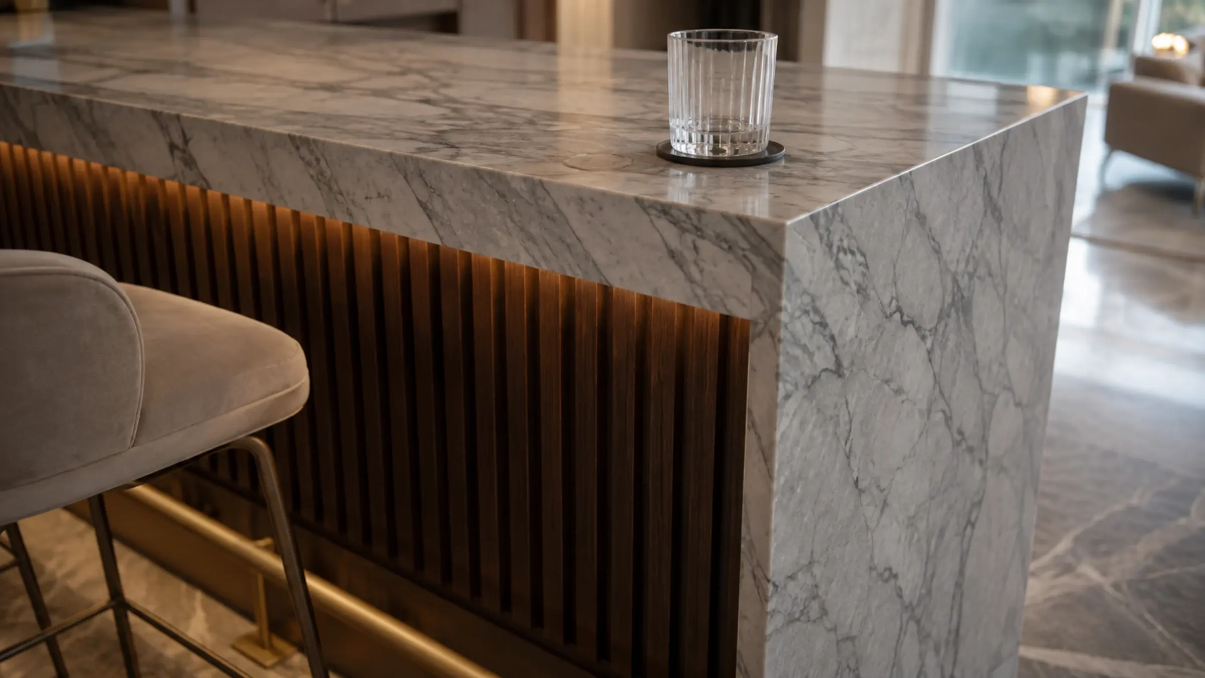 Close view of a grey-veined marble waterfall bar counter over dark fluted walnut with a brass footrail