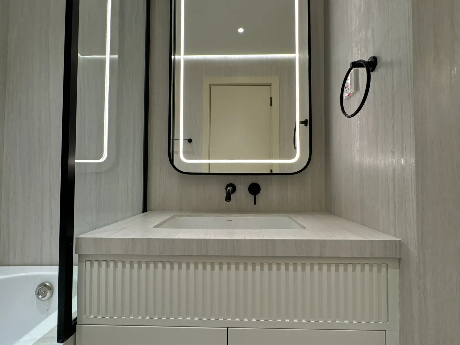 Fluted vanity unit under a backlit mirror with matte black taps
