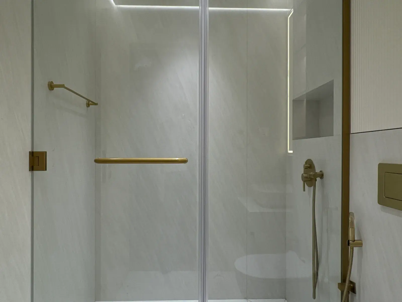 Walk-in shower behind a frameless screen with brushed gold fittings