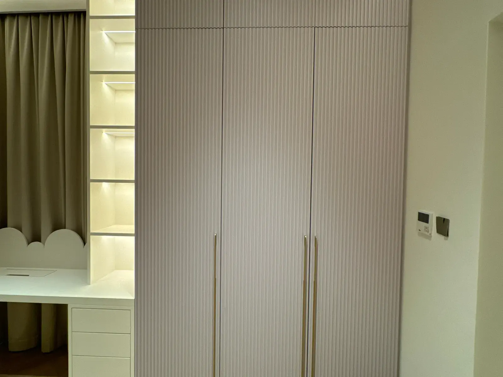 Fluted wardrobe doors beside a lit dressing table with drawers