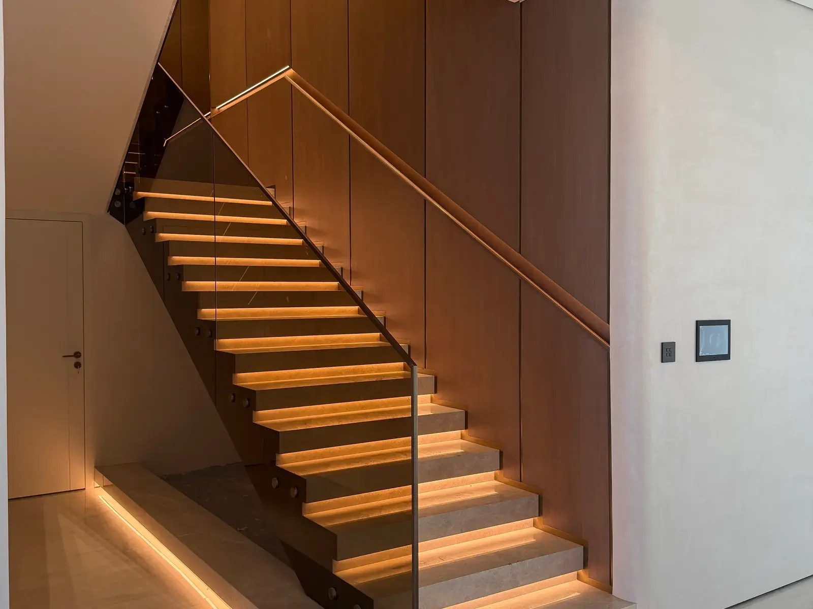 Floating timber staircase with lit risers against a timber-panelled wall