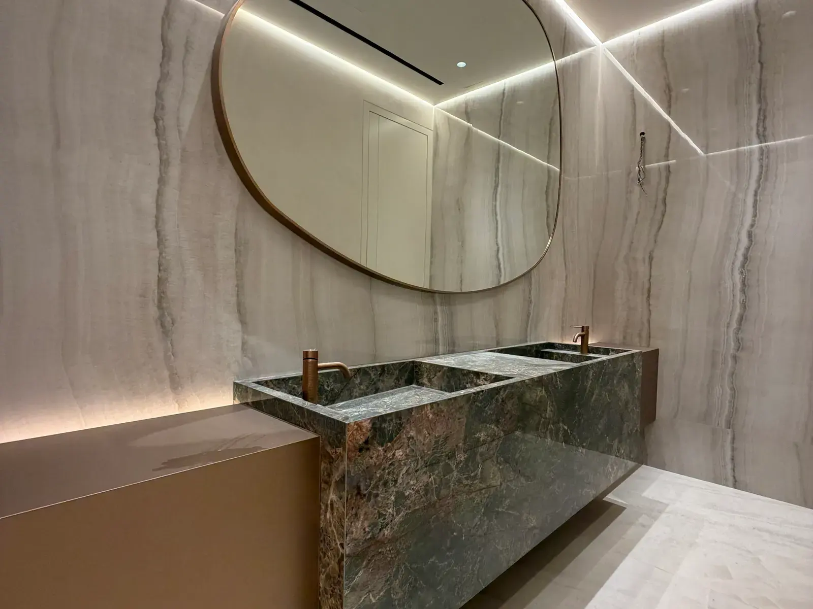 Green marble vanity with brass tap and a backlit round mirror