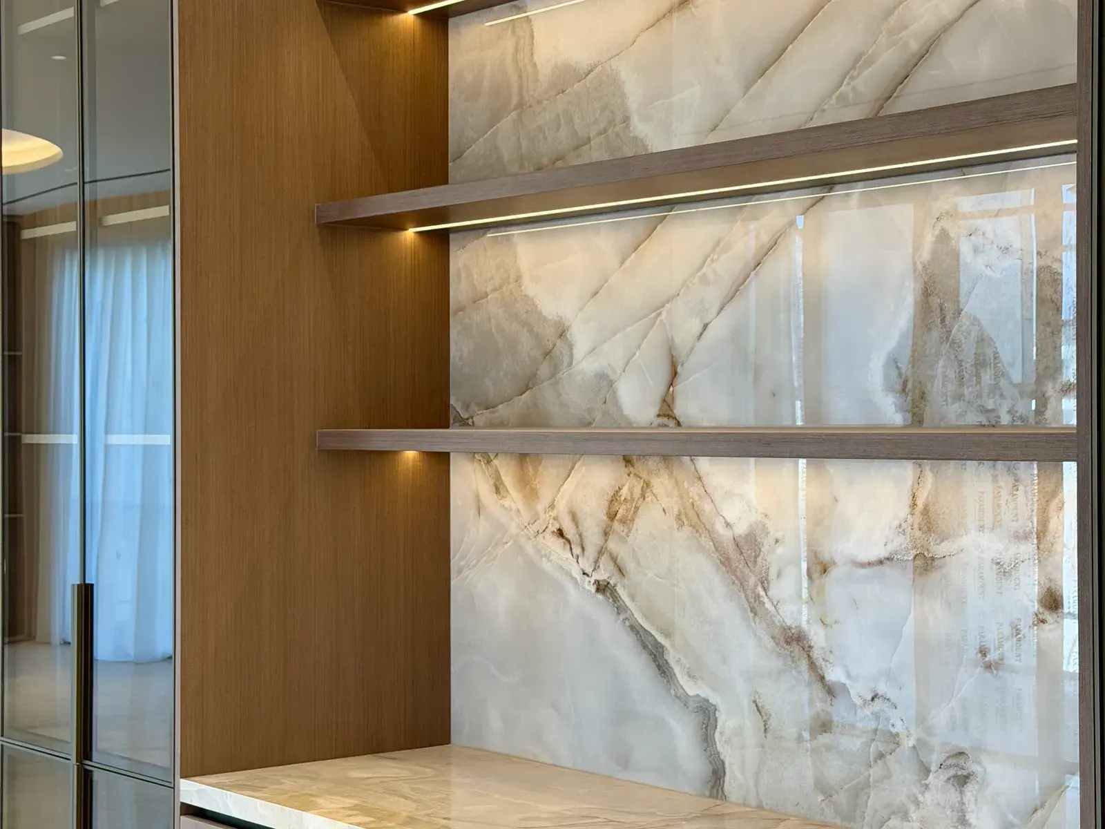 Backlit onyx panel behind slim bronze shelves
