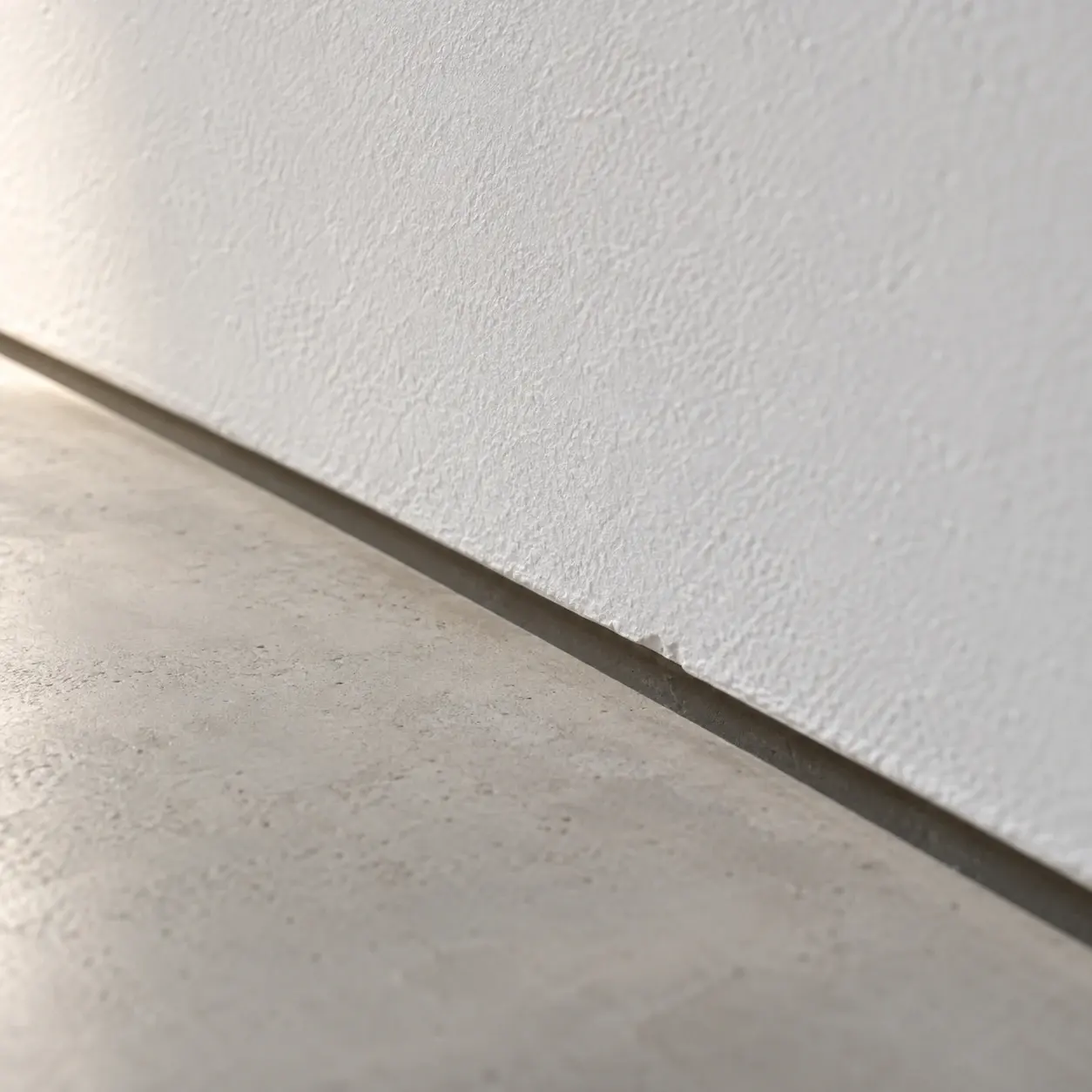 Close detail of a recessed shadow gap between a plaster wall and a seamless floor