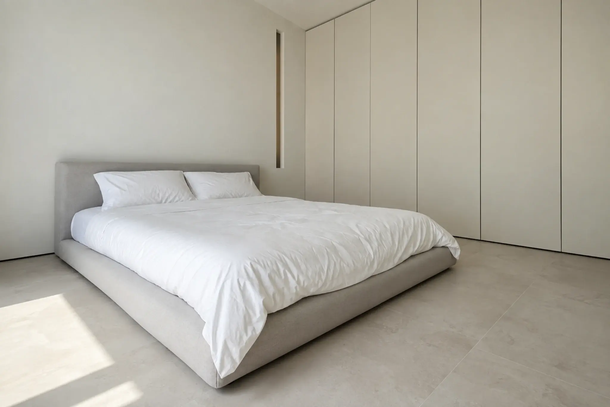 Minimalist bedroom with a low pale bed, flush handleless wardrobes and bare walls