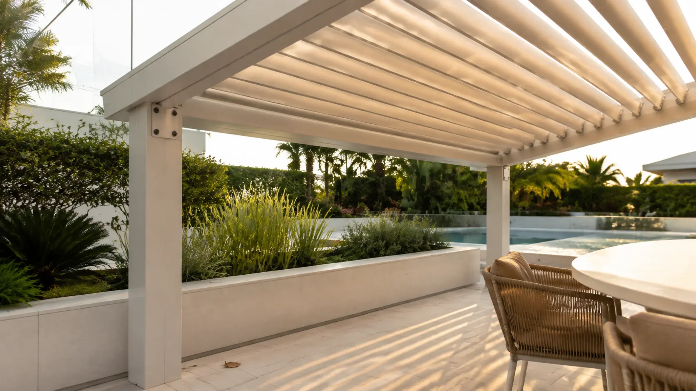 Aluminium louvred pergola over a villa terrace at golden hour with a visible bolted fixing plate at the post
