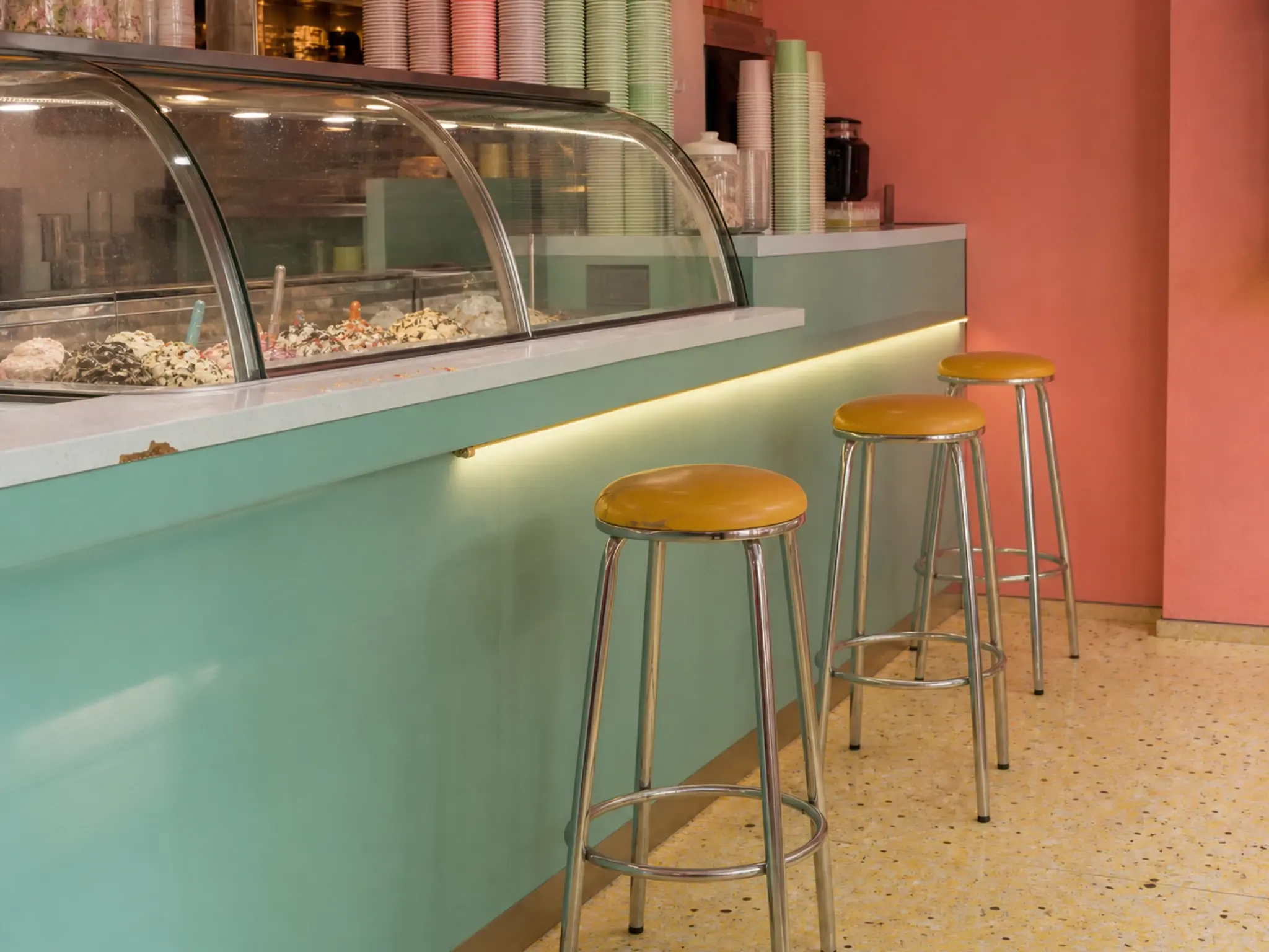 Colourful dessert parlour interior with blocked pastel and primary colour, gloss surfaces and a display counter