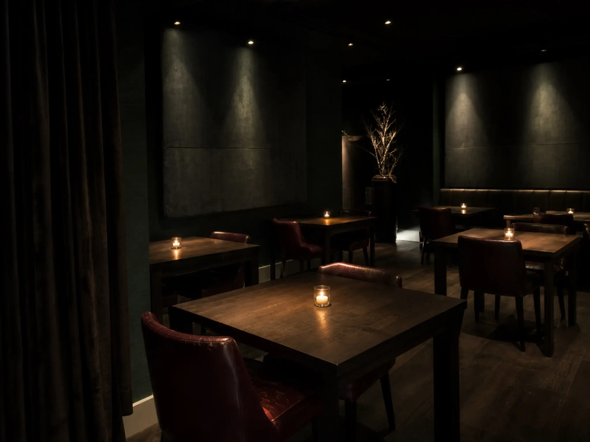 Moody fine dining room with dark walls, tightly focused table lighting and upholstered acoustics