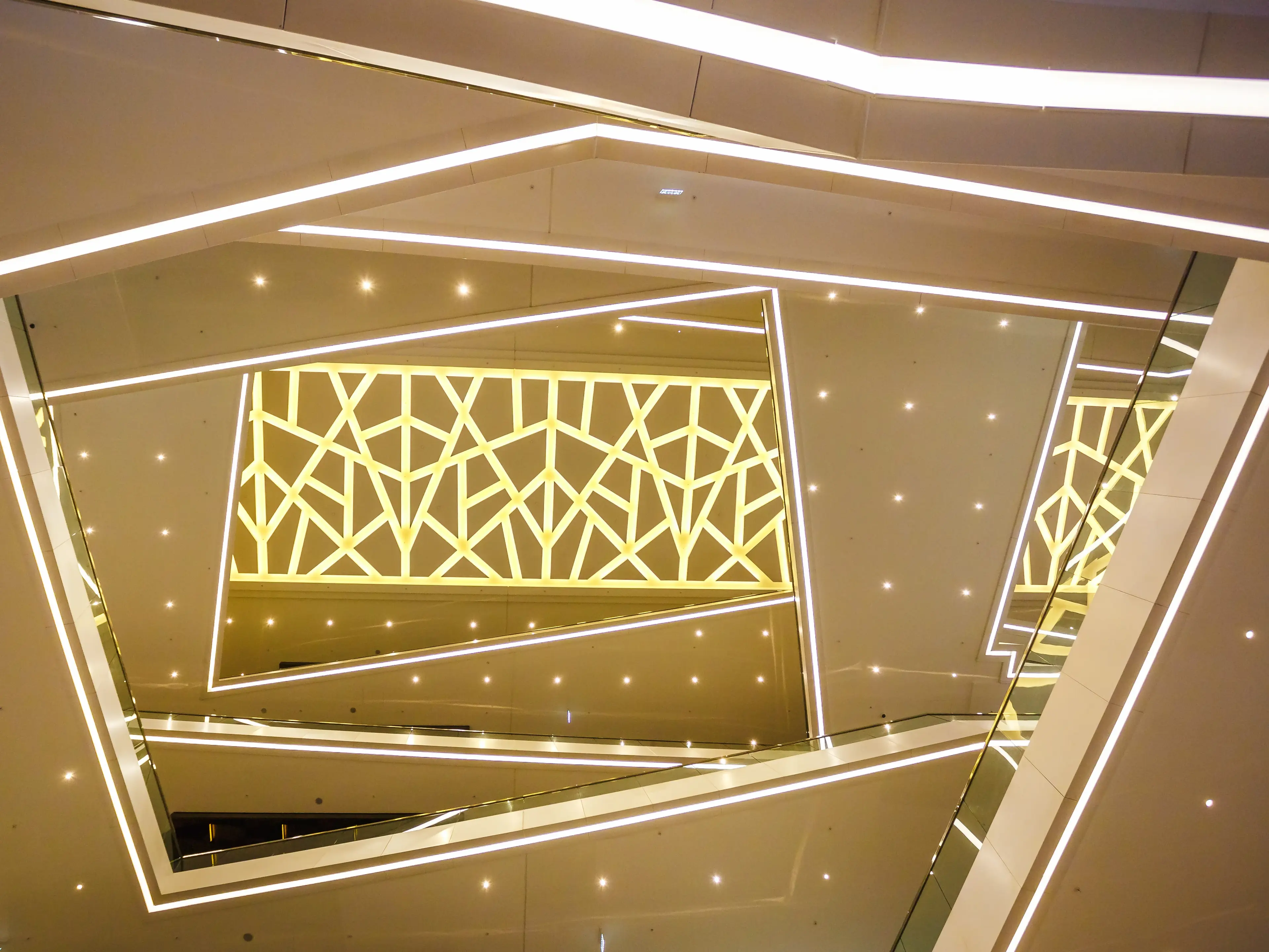 Backlit stretch ceiling in Dubai with geometric illuminated panels, gold fretwork and fibre-optic star points