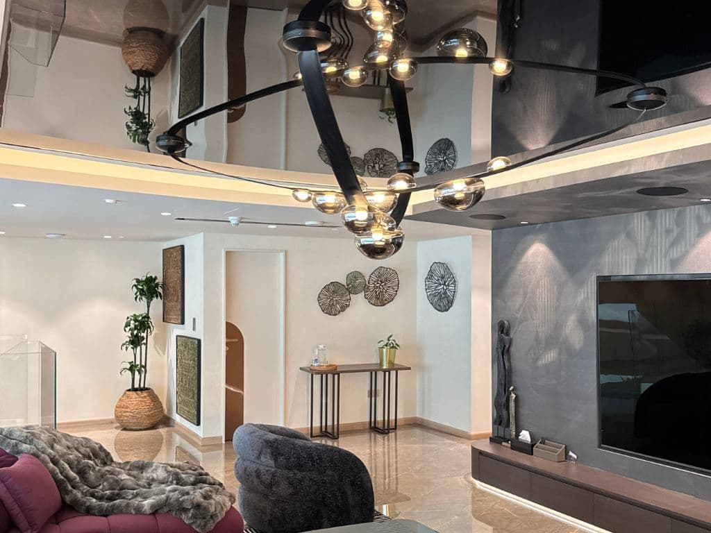 Gloss stretch ceiling reflecting a sculptural chandelier in a Dubai villa living room