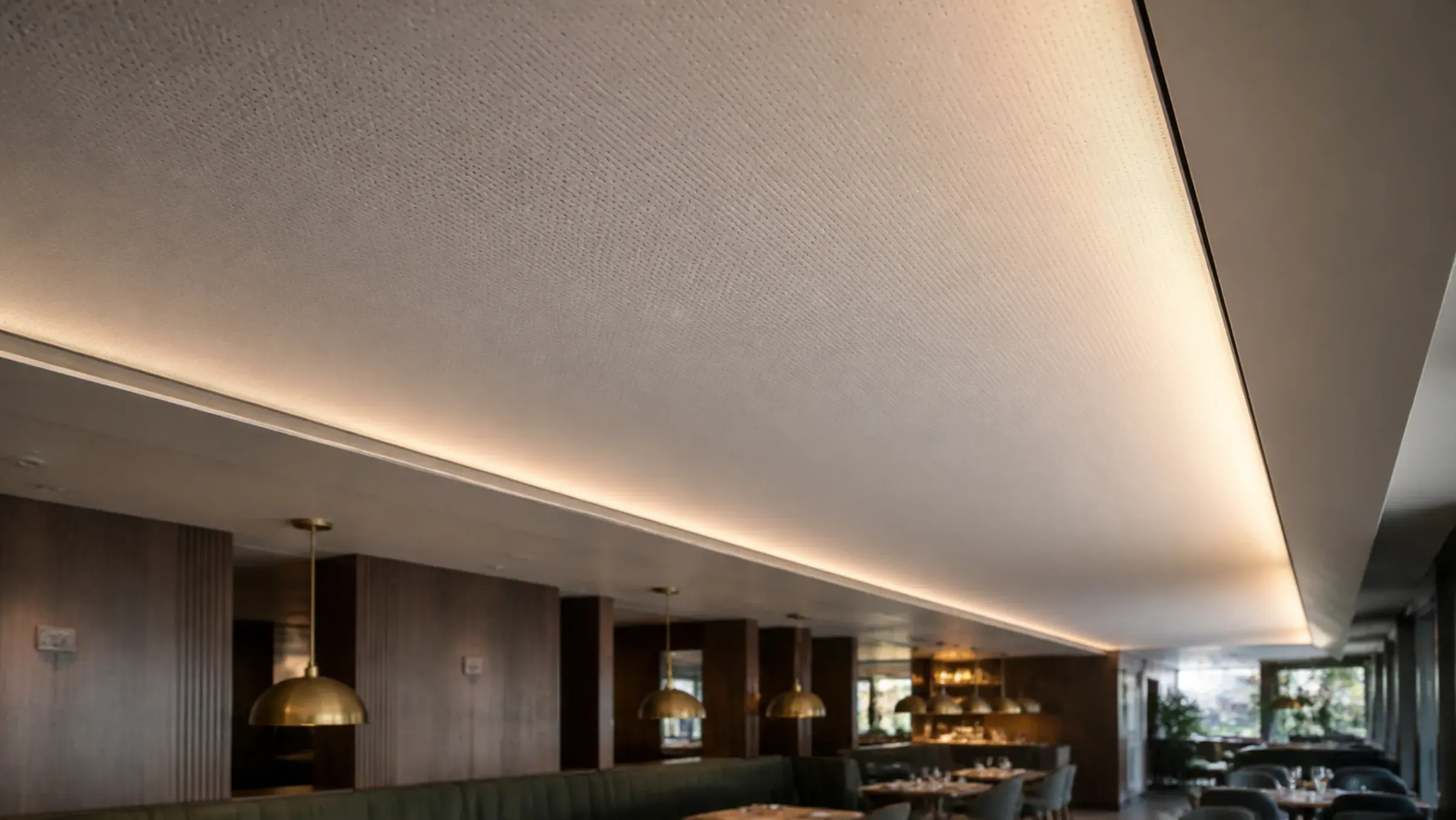 Micro-perforated acoustic stretch ceiling in a Dubai restaurant, the perforation reading as fine texture where cove light rakes across the membrane