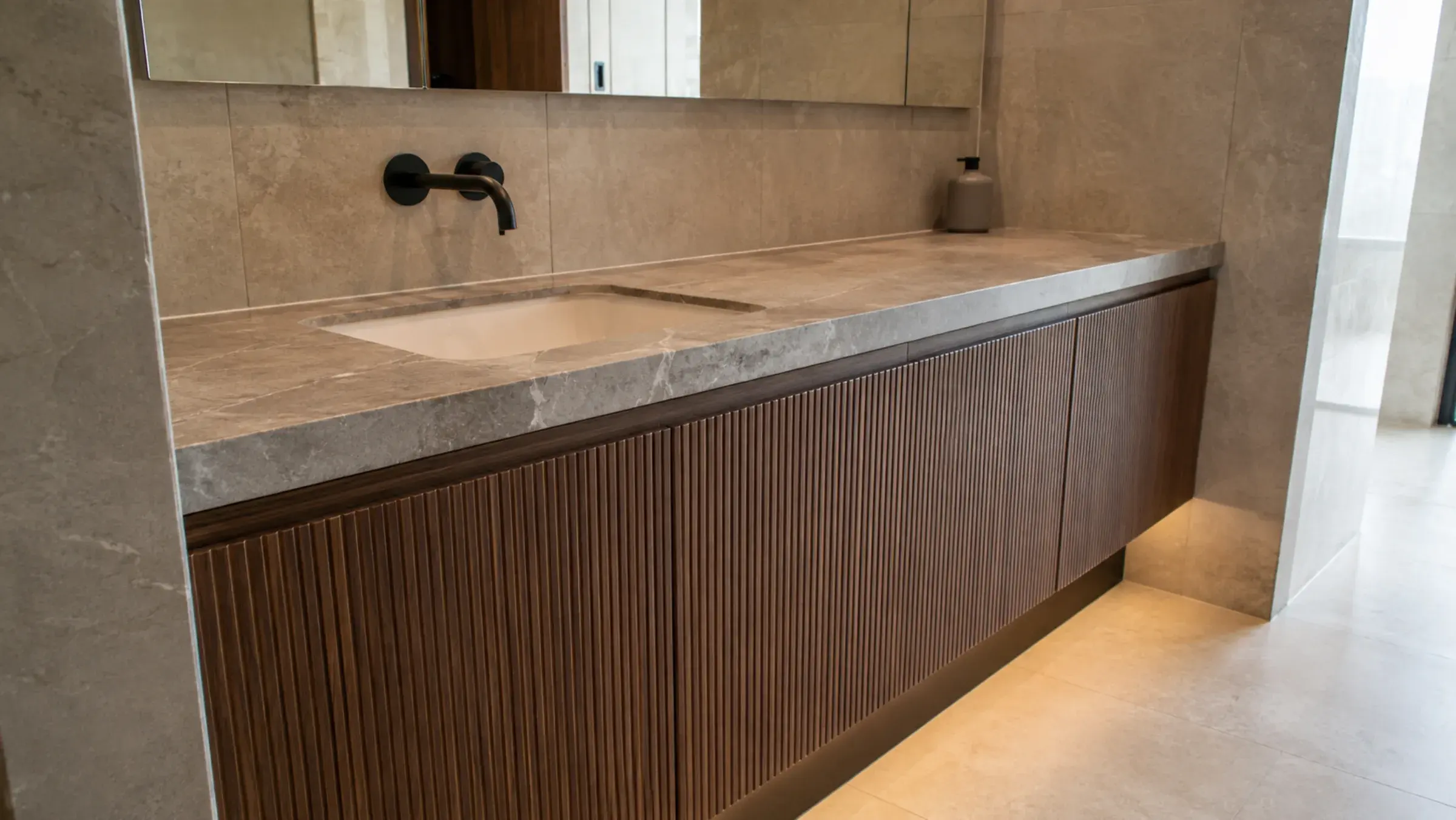 Wall-to-wall fluted walnut bathroom vanity with a marble top and recessed plinth