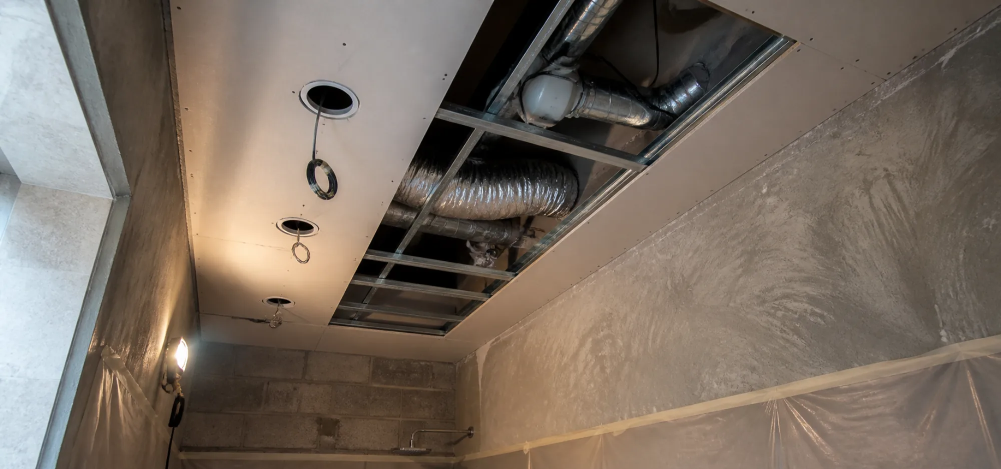 Bathroom ceiling void showing flexible extract ductwork and downlight cut-outs before boarding is closed
