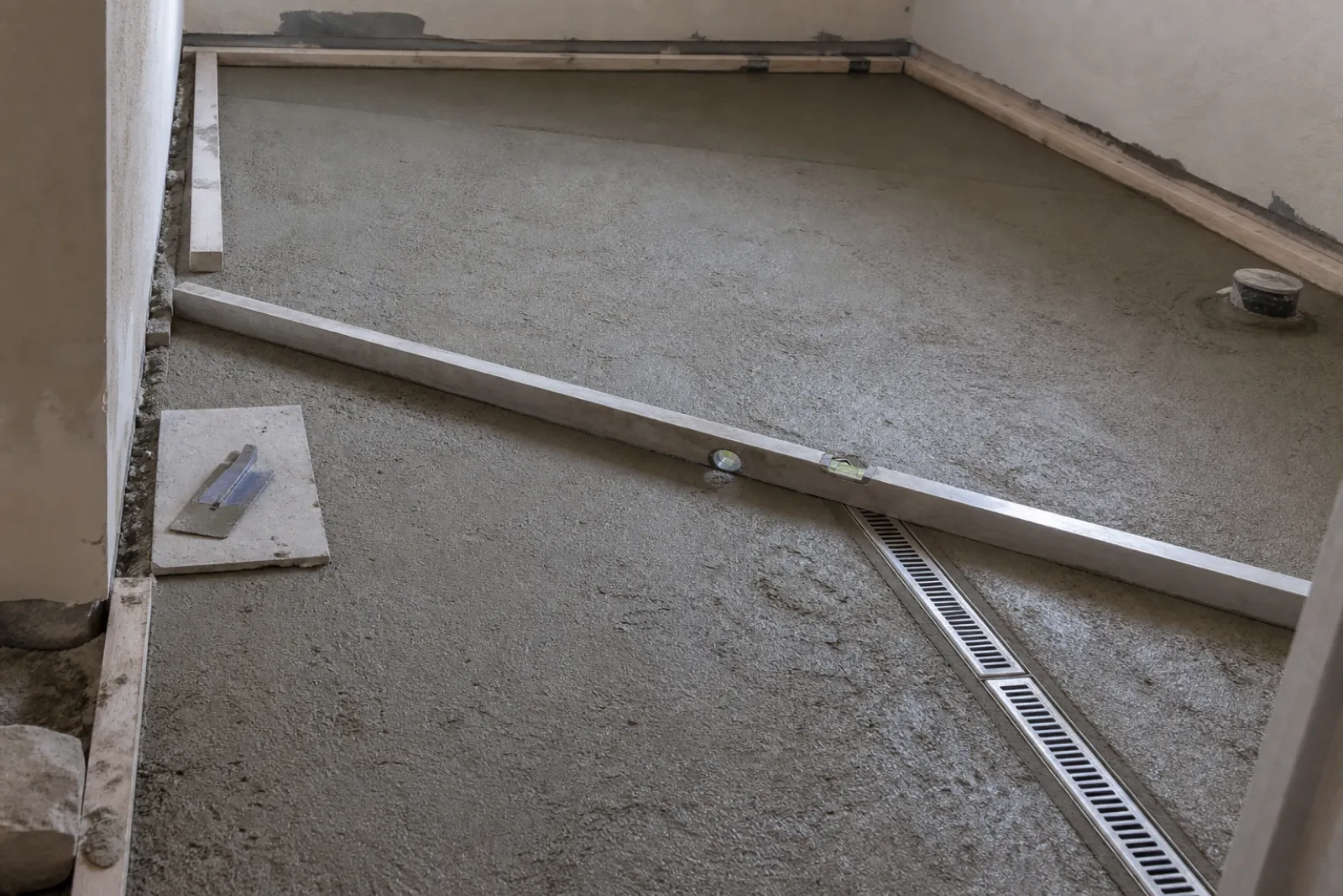 Screed formed to falls toward a linear channel drain, checked with a straightedge