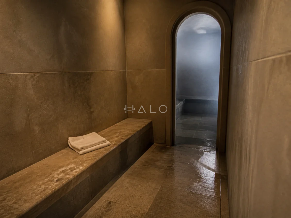 Honed-stone hammam corridor with a built-in bench, folded towel and softly lit steam